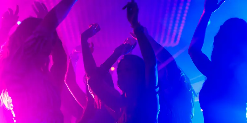 Menschen tanzen in einem Club mit bunten Lichtern.